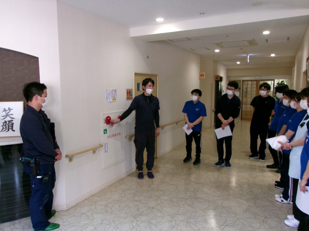廊下で複数のスタッフが集まり、説明・研修を受けている様子