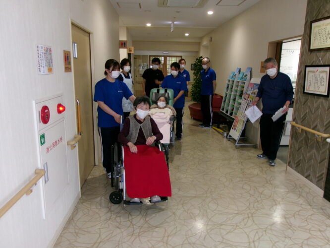 職員と入居者が廊下で活動や行事を行っている様子。車椅子の利用者も参加。