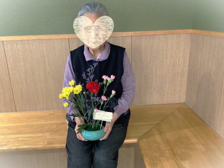 入居者が花を持って座っている風景。施設内での日常生活の一場面。